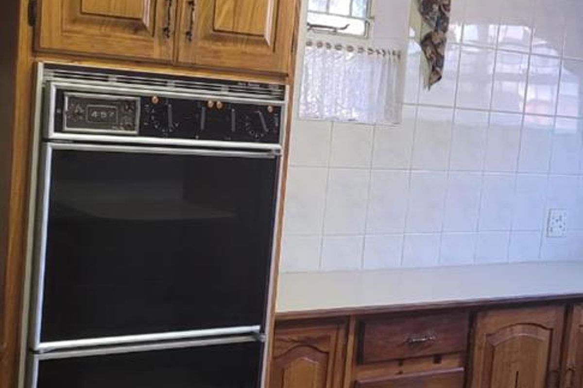 A functional kitchen featuring traditional wooden cabinetry, a built-in double oven, tiled splashbacks, and ceramic floor tiles.