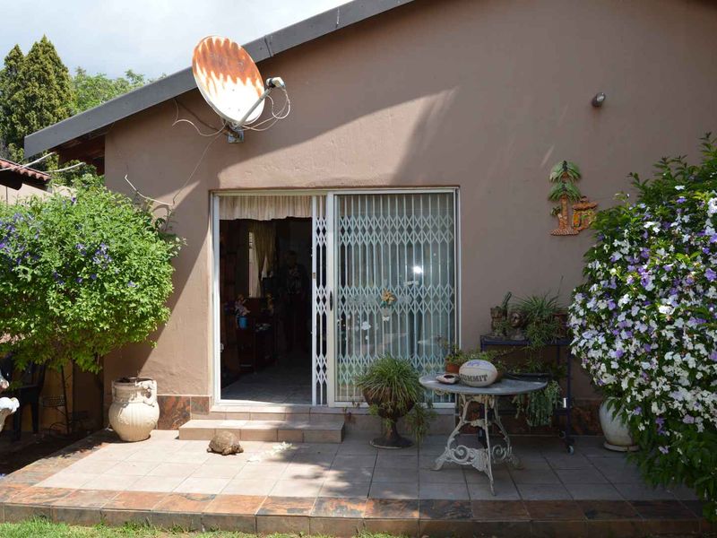 A paved patio area featuring a sliding glass door with security gate, providing direct access to the home's interior.