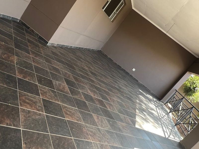 A spacious covered patio area featuring dark tiled flooring and a metal balustrade, offering a clean and functional outdoor living space.