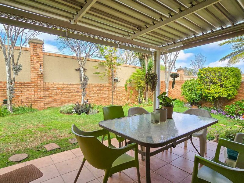 A covered patio area featuring tiled flooring and a corrugated metal roof, overlooking a private garden enclosed by a brick boundary wall.