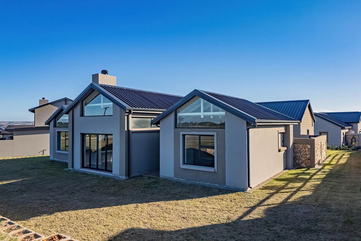 A modern rear exterior view of the house featuring a pitched metal roof, large glass windows, and a well-maintained lawn.