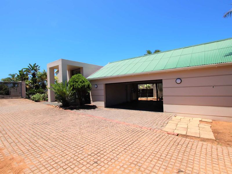 Front exterior view of the property featuring a paved driveway, a garage, and a distinctive green corrugated metal roof.