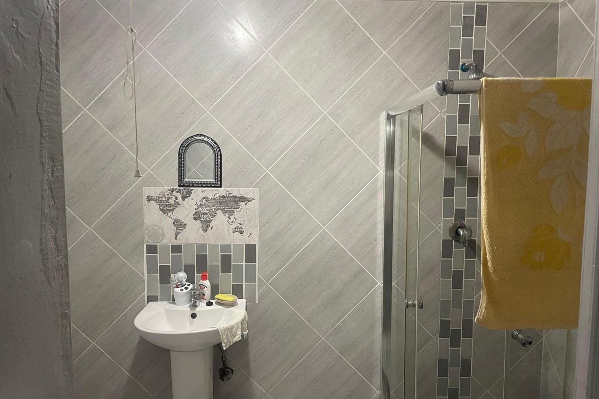 A functional bathroom featuring a pedestal basin, a glass-enclosed shower, and grey diamond-patterned wall tiling.