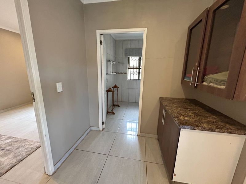 A functional laundry area featuring built-in cabinetry, laminate countertops, and tiled flooring, with direct access to an adjacent bathroom.
