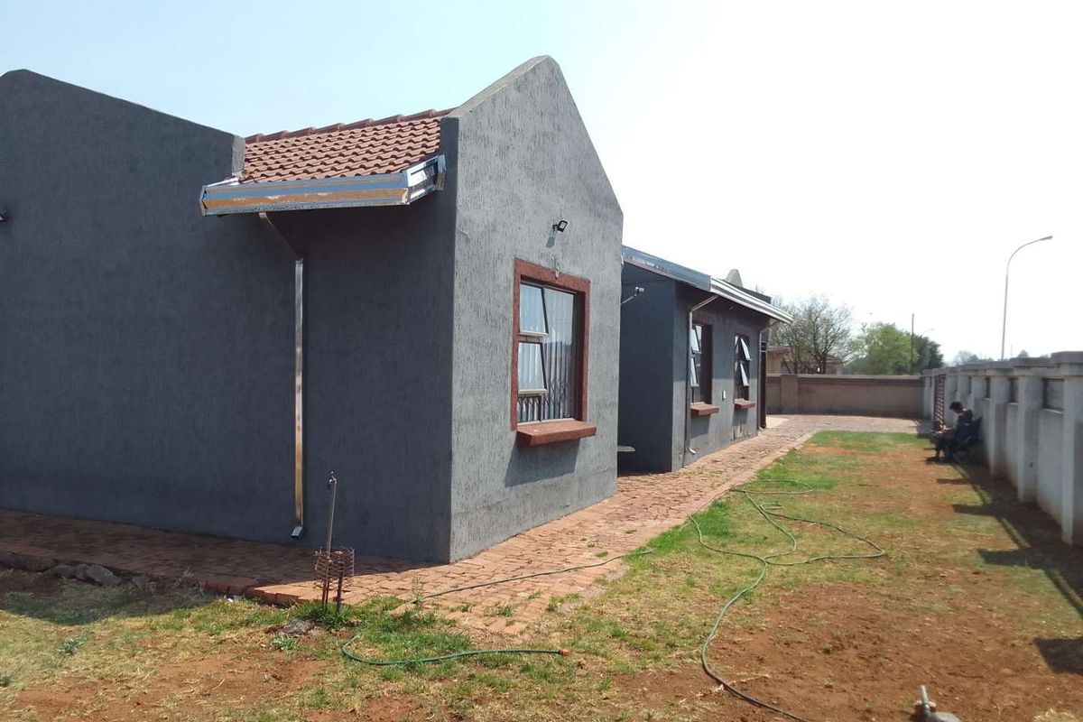 Rear view of a house featuring a textured grey facade, terracotta roof tiles, and a brick paved walkway leading along the side of the property.