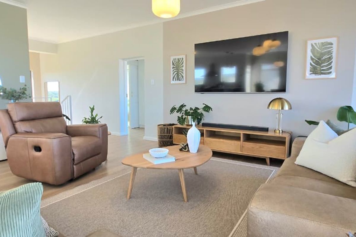 A bright and spacious living room featuring neutral tones, modern light fixtures, and large windows that provide ample natural light.