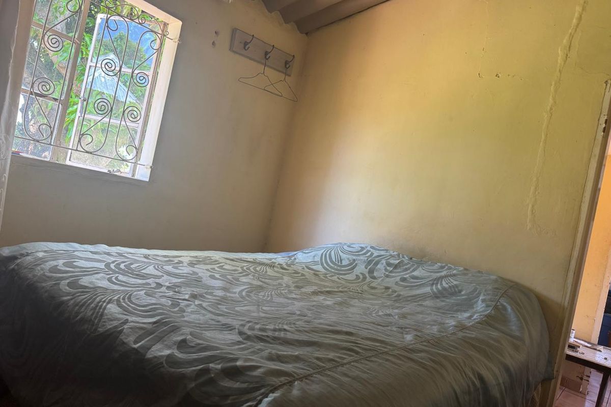A bedroom featuring security bars on the window and an exposed corrugated ceiling, requiring cosmetic updates to the wall finishes.
