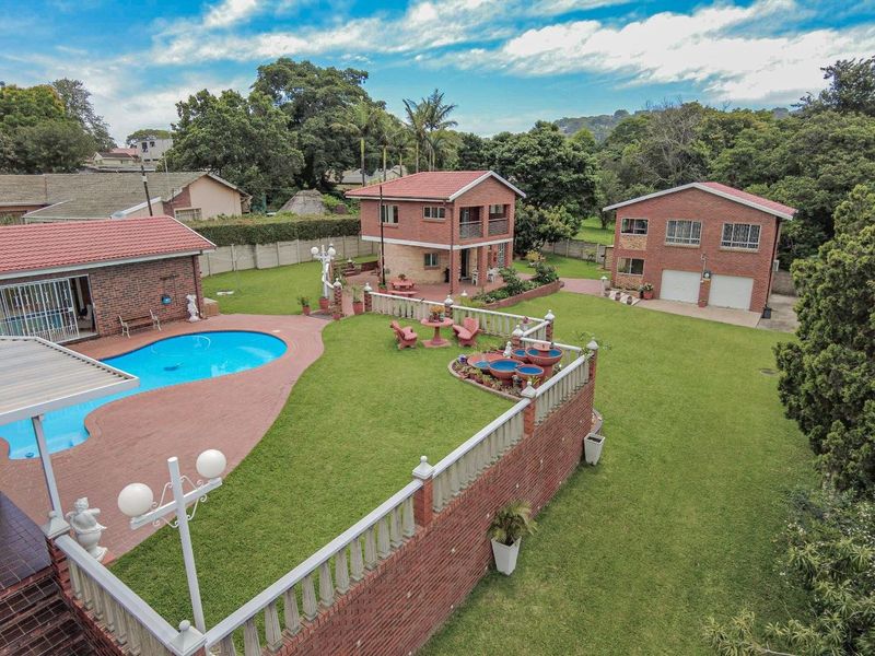 Aerial view of a spacious property featuring a swimming pool, large landscaped garden, double garage, and multiple brick residential structures.