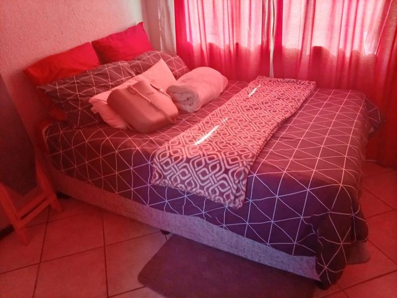 A bedroom featuring tiled flooring and window curtain rails, currently furnished with a bed.