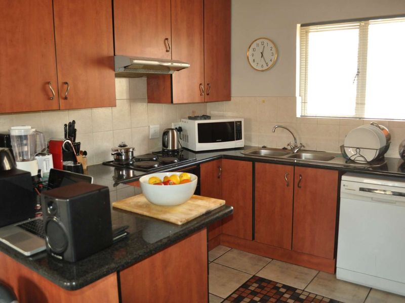 Functional kitchen featuring wood-finish cabinetry, granite countertops, a double bowl sink, and an integrated electric hob with an extractor fan.
