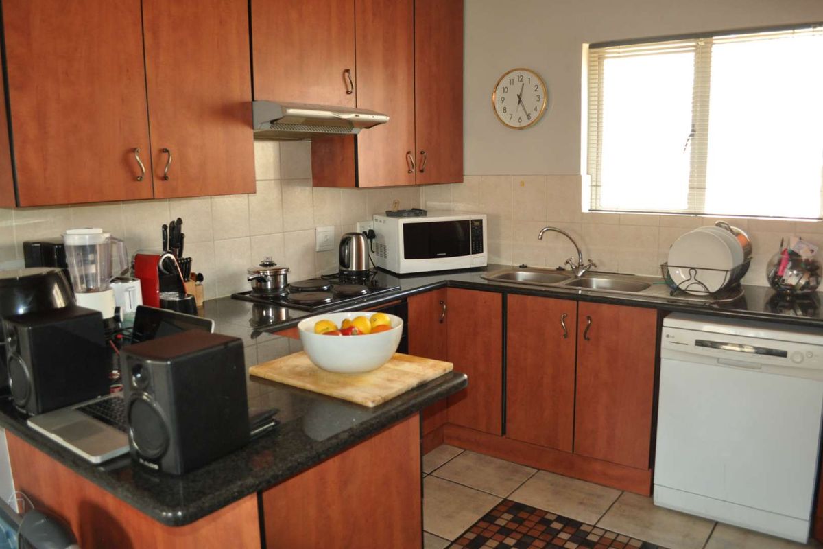 Functional kitchen featuring wood-finish cabinetry, granite countertops, a double bowl sink, and an integrated electric hob with an extractor fan.