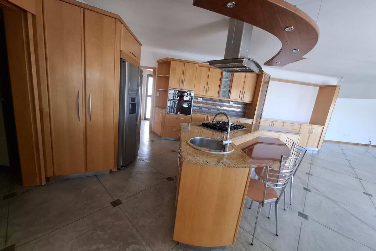 Spacious kitchen featuring light wood cabinetry, granite countertops, a central island with a built-in gas hob, and a stainless steel extractor fan.