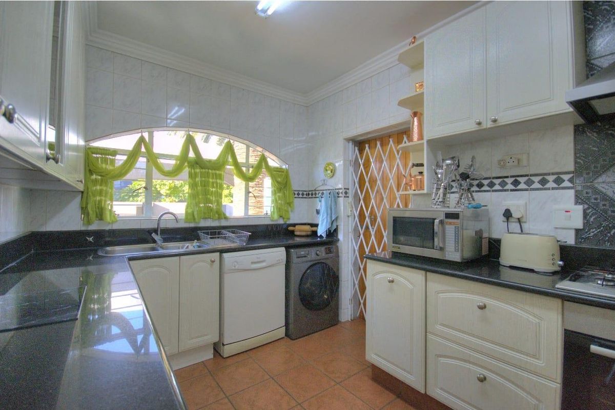 A functional kitchen featuring granite countertops, white cabinetry, tiled walls, and an arched window, providing a practical workspace with integrated appliance connections.