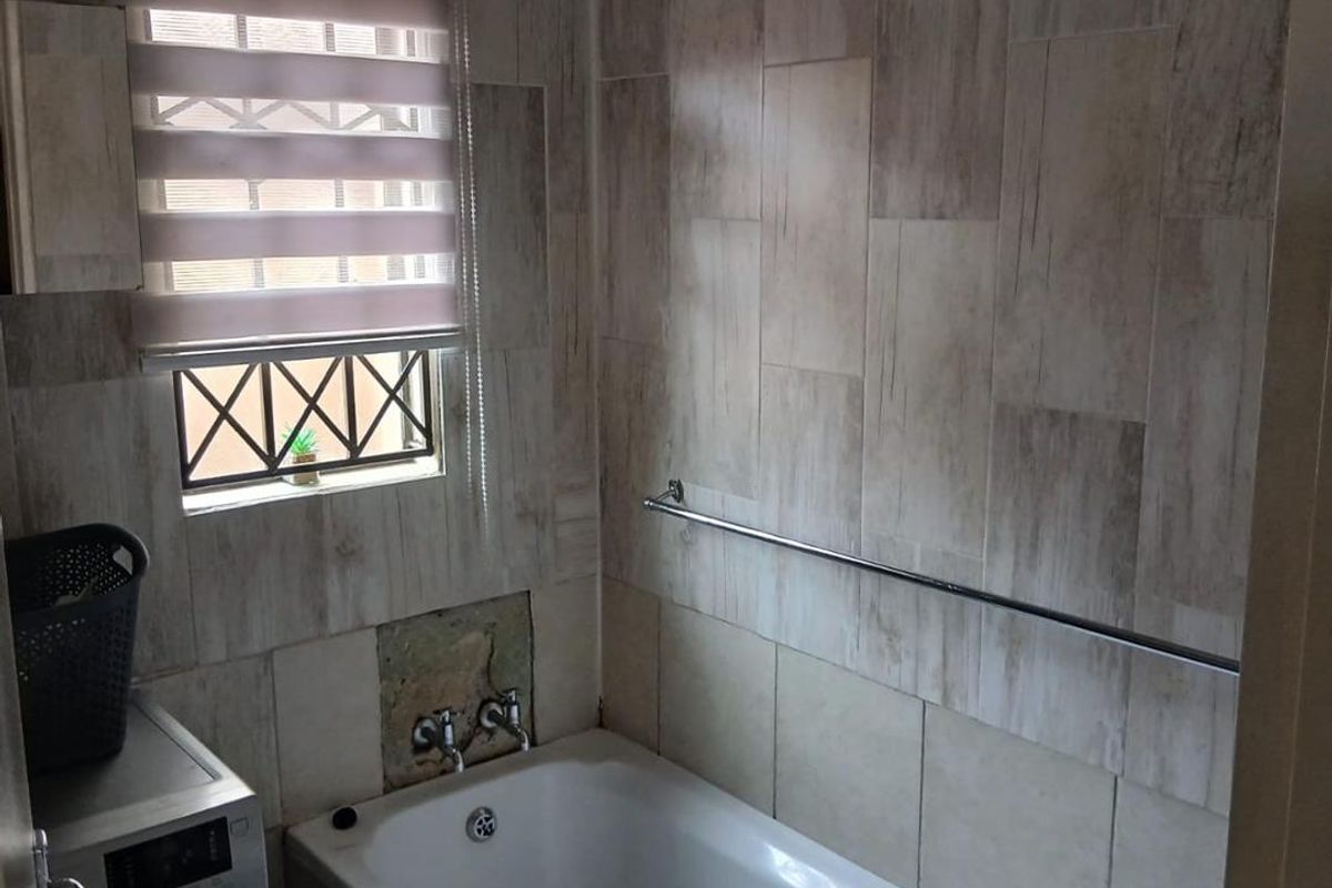 A bathroom featuring a bathtub with wall-mounted faucets, wood-look wall tiling, and a window with a roller blind.