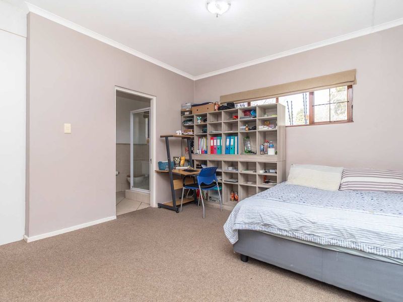 A spacious bedroom featuring neutral wall tones, carpeted flooring, and an attached en-suite bathroom, offering a functional and comfortable living space.