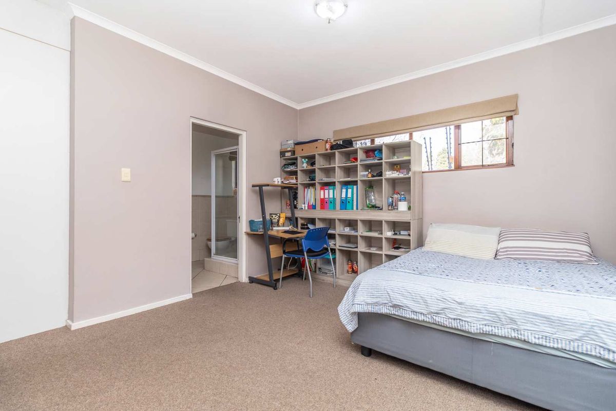 A spacious bedroom featuring neutral wall tones, carpeted flooring, and an attached en-suite bathroom, offering a functional and comfortable living space.