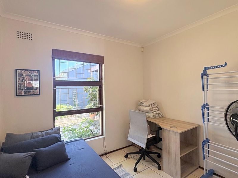 A functional bedroom featuring tiled flooring, a window with security bars, and neutral wall finishes, suitable for use as a guest room or home office.