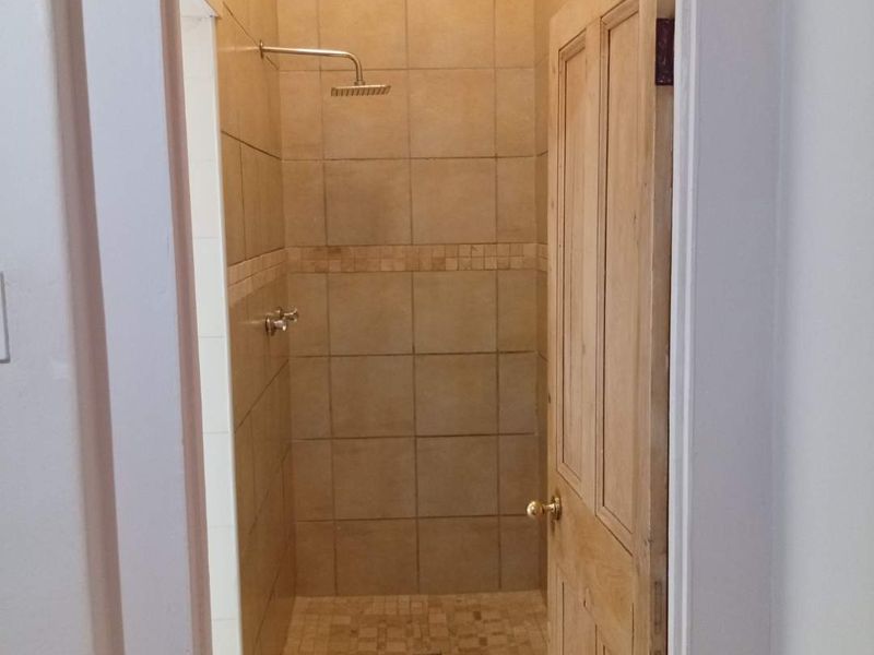 A compact shower enclosure featuring neutral wall and floor tiling, a modern rainfall shower head, and a wooden door entrance.