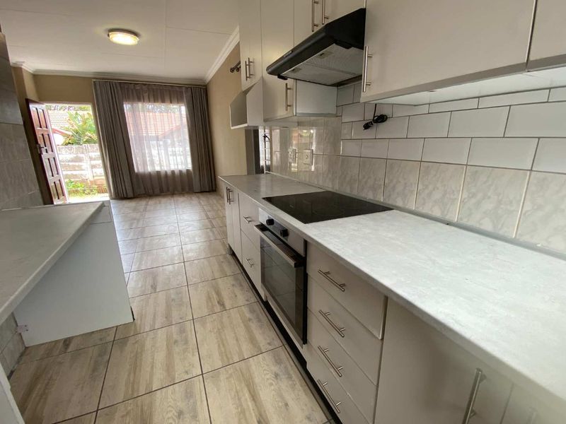 A clean, functional kitchen featuring white cabinetry, laminate countertops, built-in oven and hob, and tiled flooring, leading directly to an outdoor area.