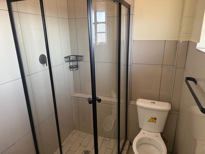 A clean, functional bathroom featuring a modern glass shower enclosure, a standard toilet, and neutral wall tiling.
