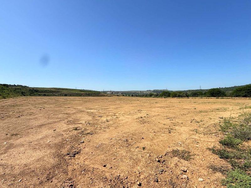A wide, undeveloped plot of land featuring open terrain and natural vegetation under a clear blue sky.