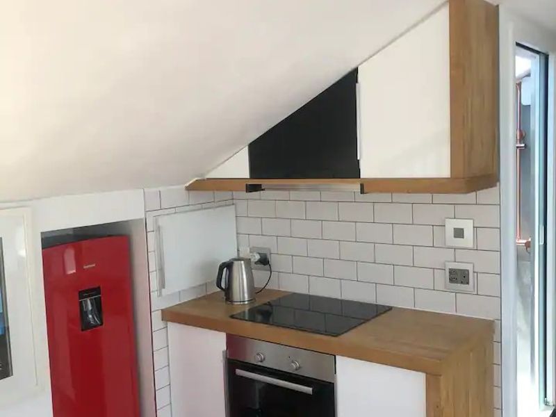 Compact kitchen featuring a built-in oven, electric hob, wooden countertops, and white subway tile backsplash, designed to fit under a sloped ceiling.
