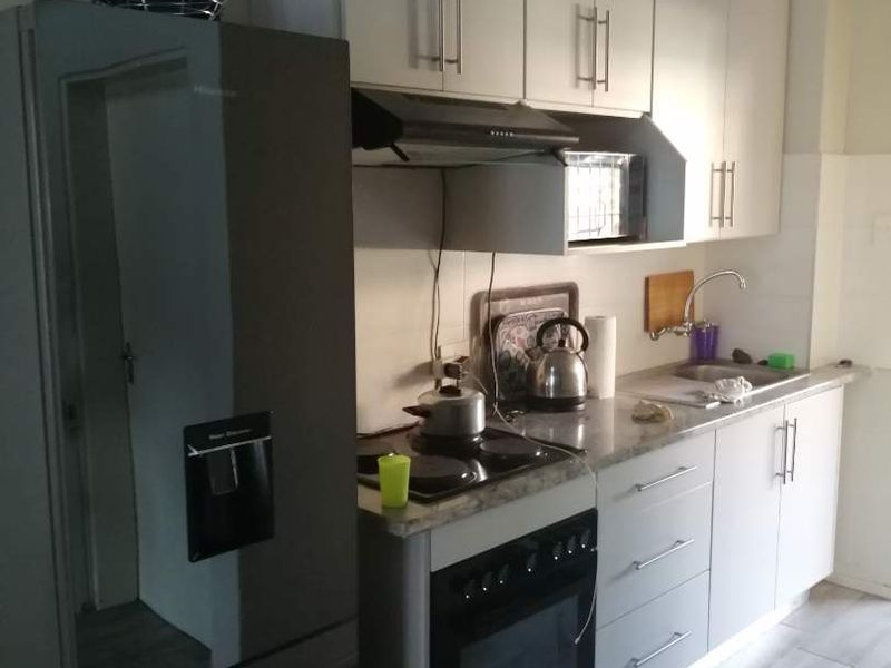 A functional kitchen featuring built-in cabinetry, laminate countertops, an electric oven with hob, and tiled flooring.