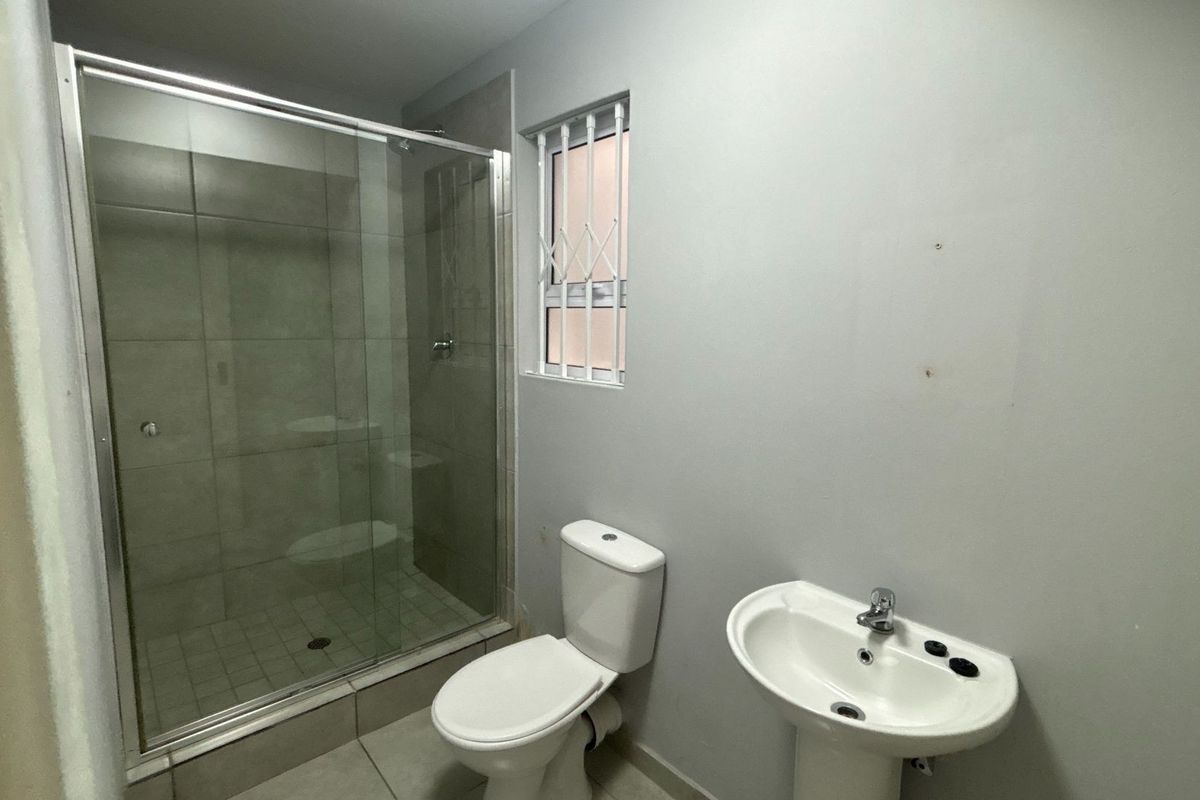 A functional bathroom featuring a glass-enclosed shower, a pedestal basin, and a toilet, finished with neutral floor and wall tiling.