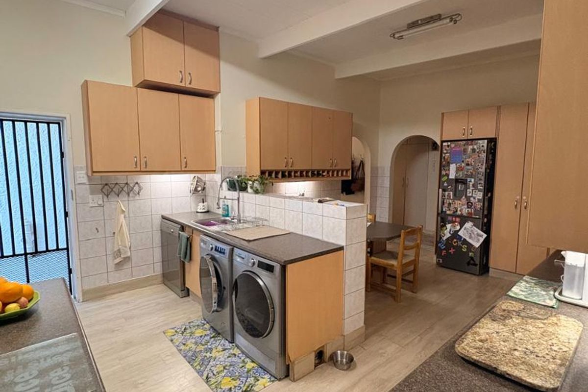 Functional kitchen featuring laminate cabinetry, tiled backsplash, and integrated laundry appliances, with an open-plan layout connecting to the dining area.