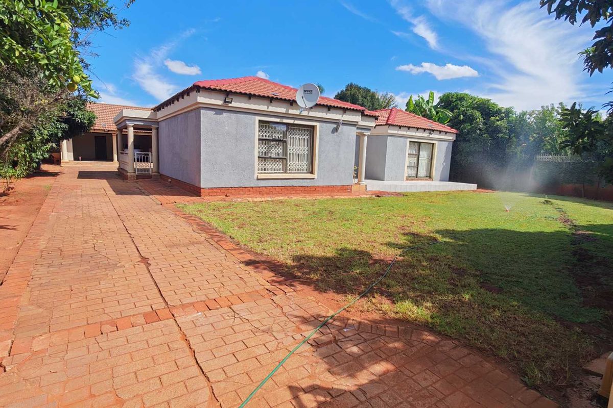 Exterior view of the house featuring a paved driveway, tiled roof, and a spacious garden area with established trees.