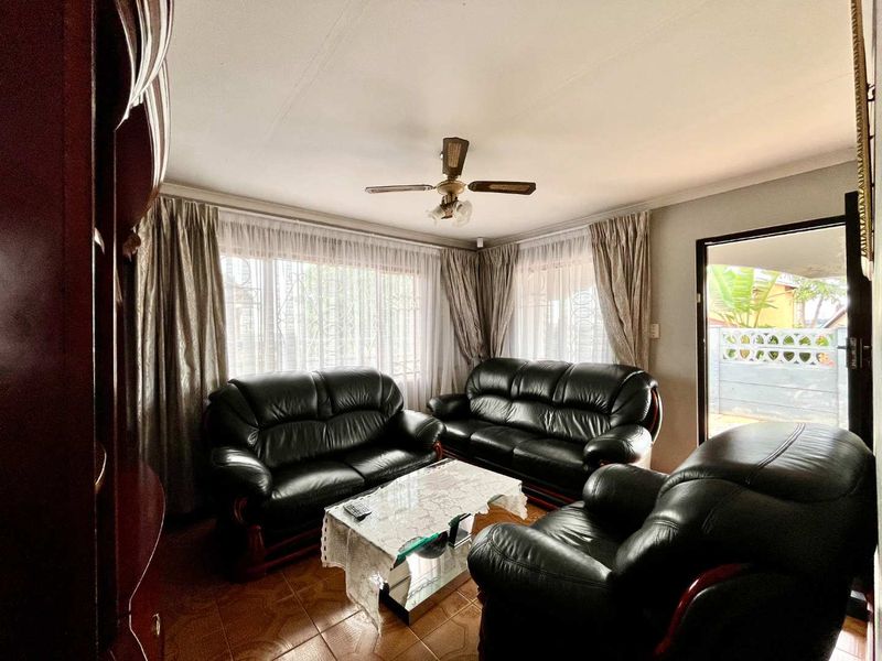 A comfortable living room featuring tiled flooring, a ceiling fan, and large windows with security bars, providing natural light and access to the exterior.