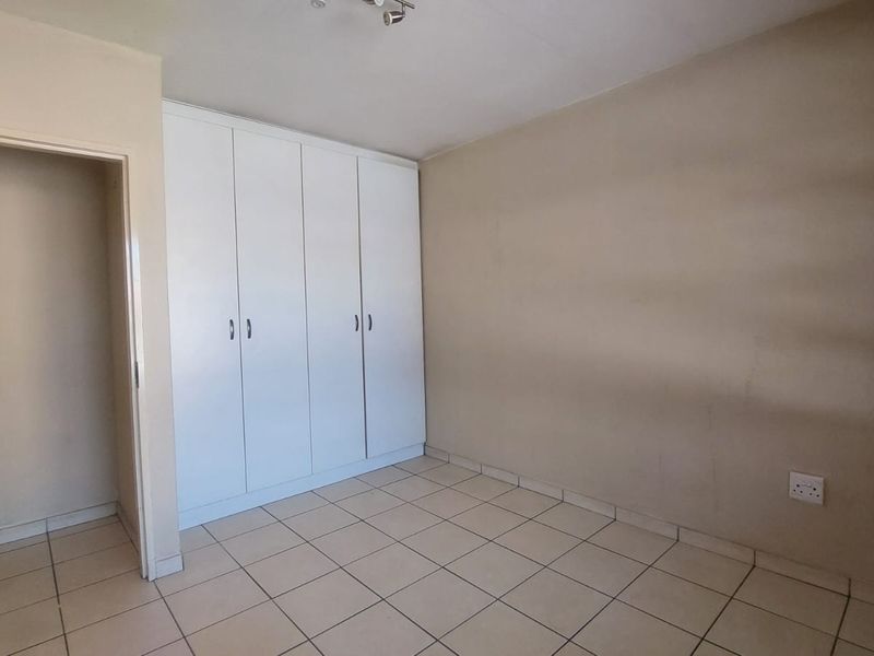 A clean, empty bedroom featuring neutral tiled flooring and white built-in cupboards, offering a blank canvas for personalization.