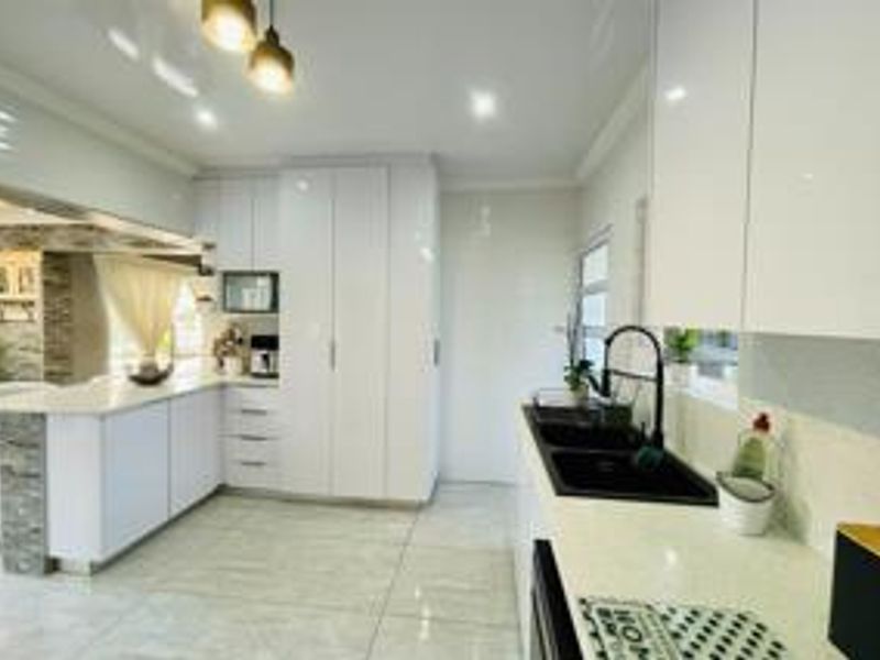 Modern kitchen featuring high-gloss white cabinetry, stone countertops, a double basin sink with black fixtures, and elegant tiled flooring.