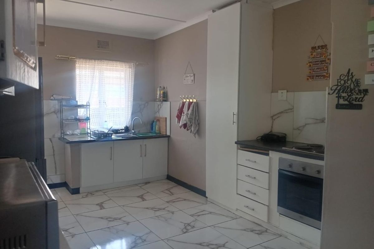 A functional kitchen featuring white cabinetry, marble-look tiled flooring and splashbacks, a built-in oven, and a hob with ample storage space.