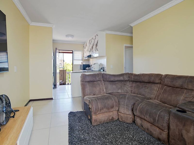 Open-plan living area featuring tiled floors, cornice detailing, and a functional kitchen space with built-in cabinetry and appliances, leading to an outdoor balcony.