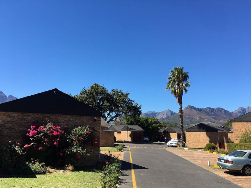 Exterior view of a residential apartment complex featuring brick facades, paved driveways, and scenic mountain views in the background.