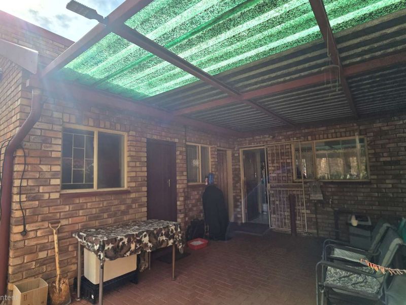 A covered outdoor patio area featuring face brick walls, paved flooring, and a corrugated roof with shade netting, providing a functional sheltered space.