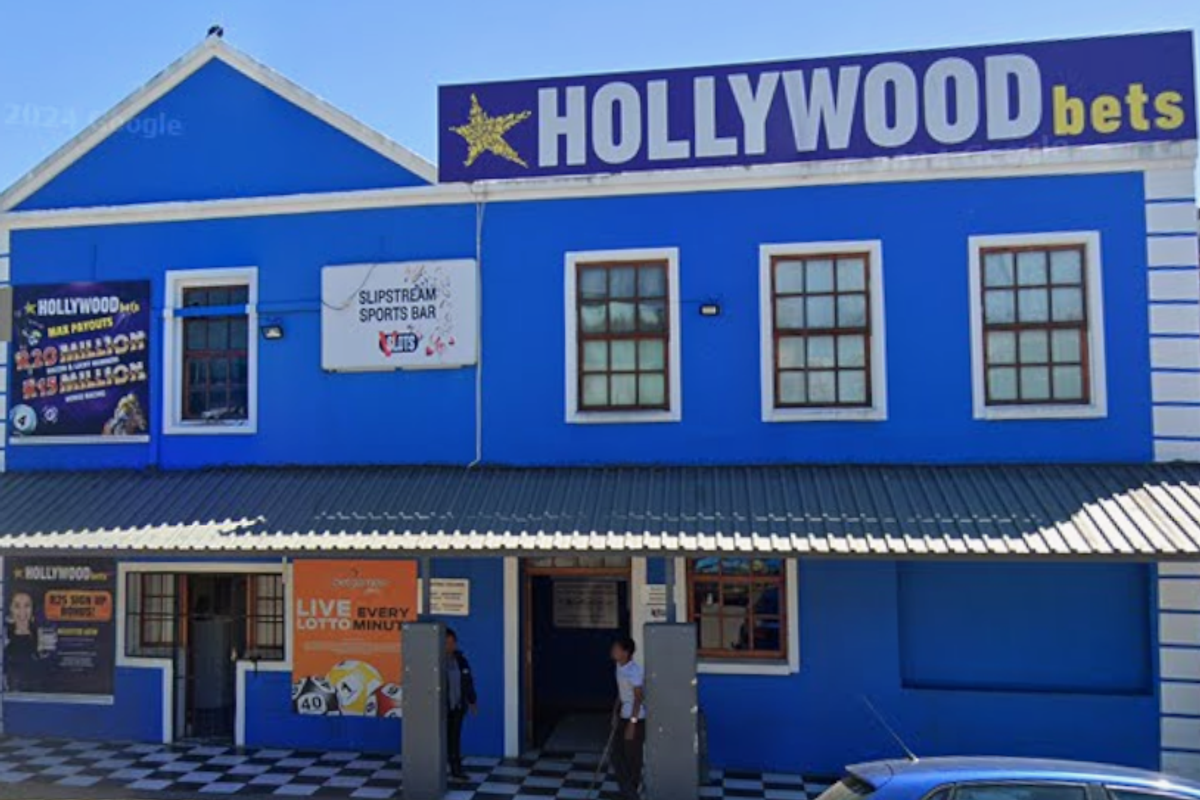 Front facade of a commercial mixed-use building featuring blue exterior paint, corrugated roofing, and prominent signage for a sports betting establishment.
