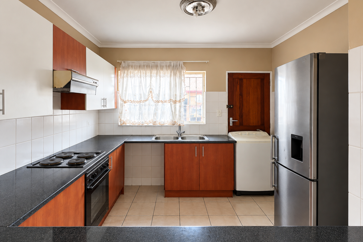 A functional kitchen featuring wood-finish cabinetry, granite countertops, a built-in oven and hob, and tiled flooring with a dedicated space for laundry appliances.
