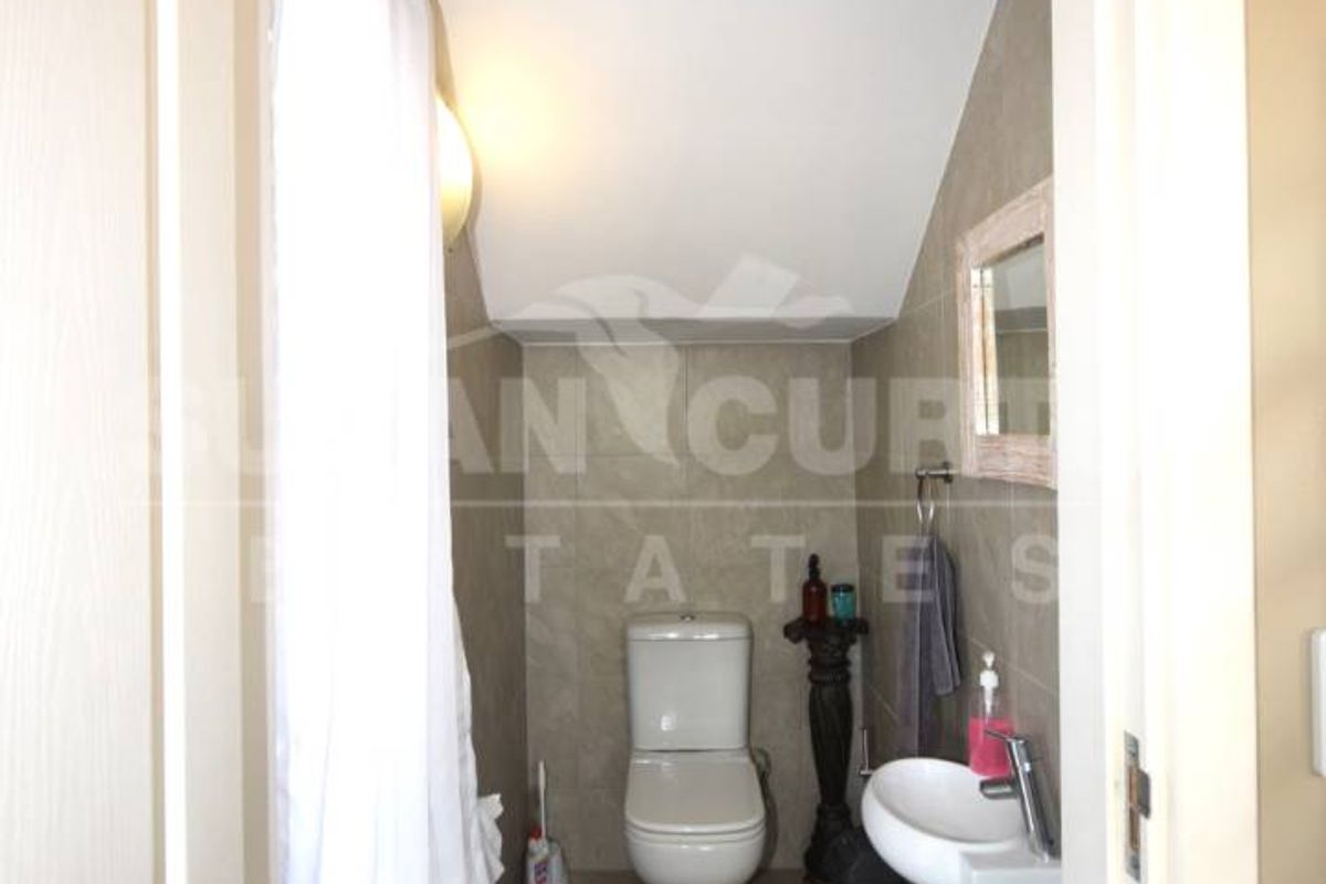 A compact bathroom featuring a wall-mounted basin, a standard toilet, and tiled flooring, situated under a sloped ceiling.