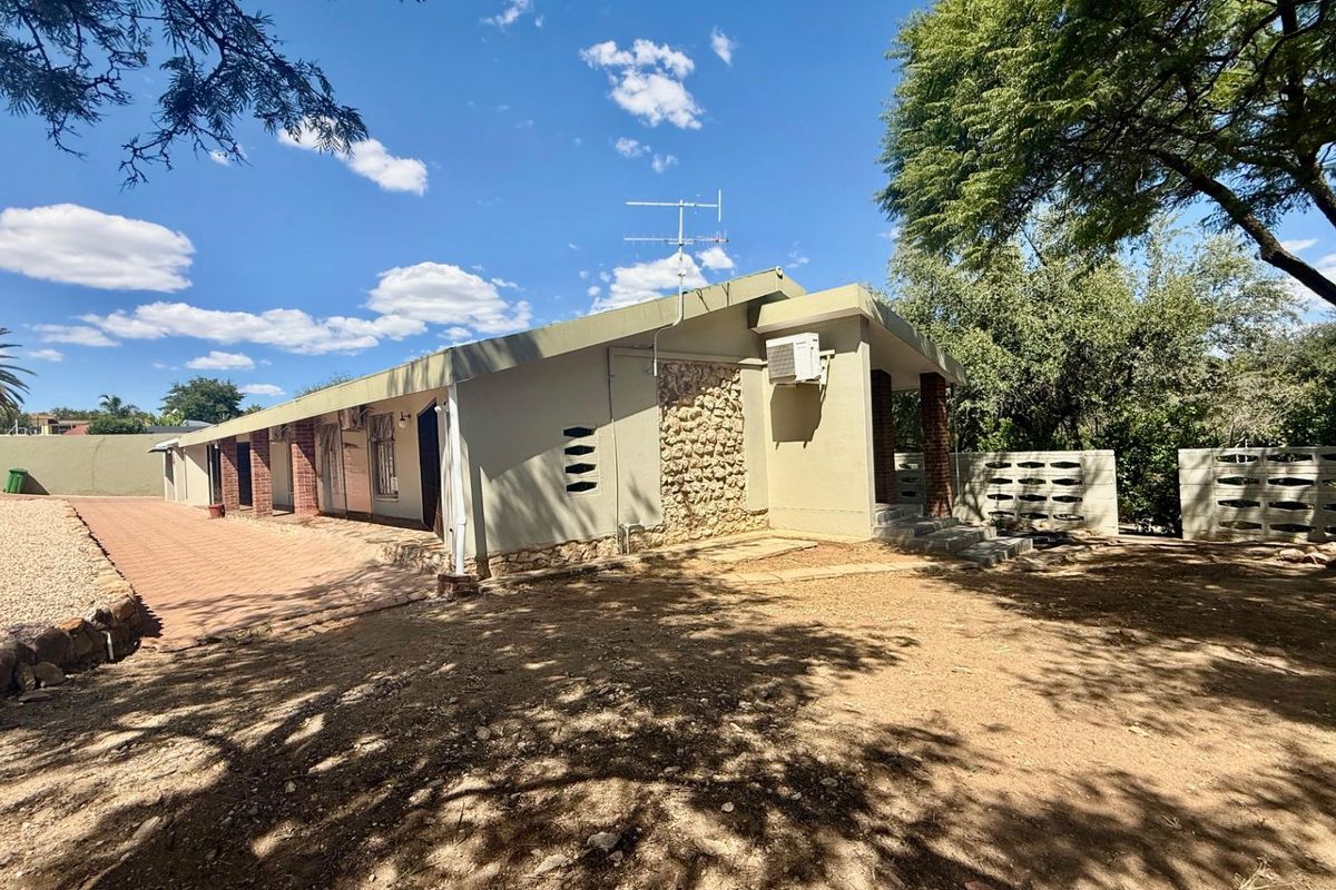 Side view of the house featuring a paved walkway, stone cladding accents, and a split-level roof design set within a spacious garden area.