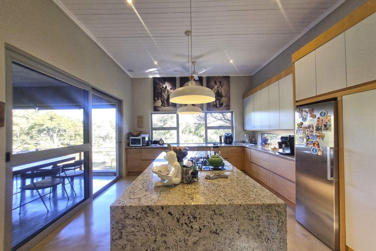 Modern kitchen featuring a large granite-topped island, sleek cabinetry, integrated appliances, and large sliding doors opening to an outdoor patio area.