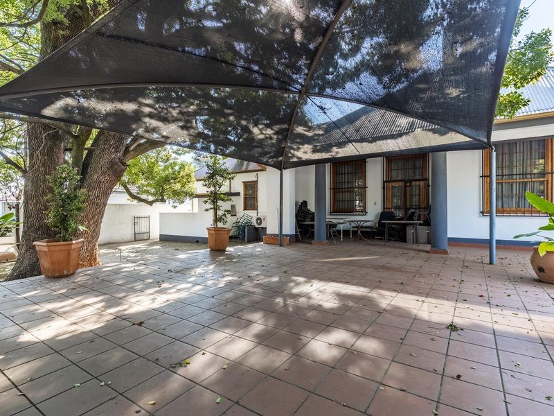A spacious outdoor patio area featuring tiled flooring, structural support columns, and a large overhead shade sail, providing a functional covered exterior space.