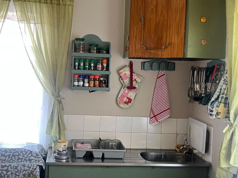 A compact kitchen area featuring a stainless steel sink, tiled splashback, and dated wall-mounted cabinetry.