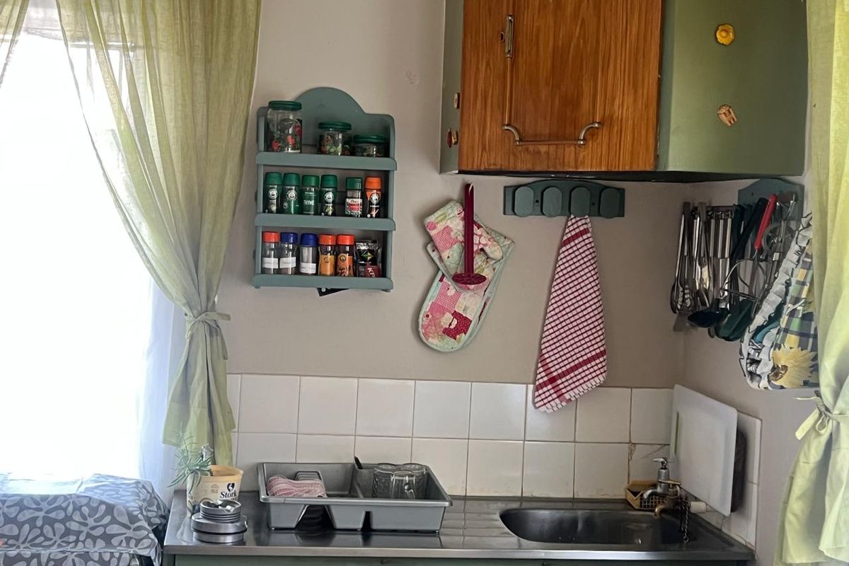 A compact kitchen area featuring a stainless steel sink, tiled splashback, and dated wall-mounted cabinetry.