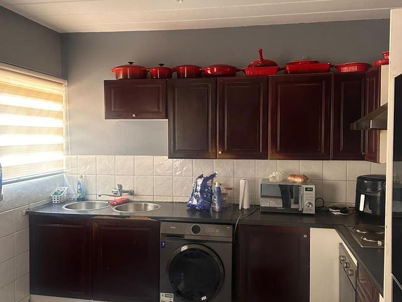 A functional kitchen featuring dark wood cabinetry, a double basin sink, tiled backsplash, and integrated appliances, offering potential for modernization and aesthetic improvement.