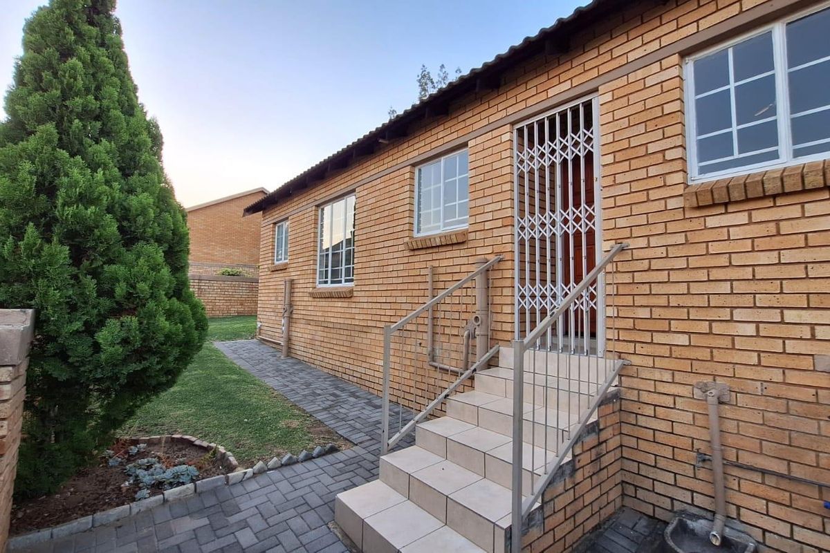 Exterior view of a brick townhouse featuring a paved walkway, tiled entrance steps with security gate, and well-maintained garden area.
