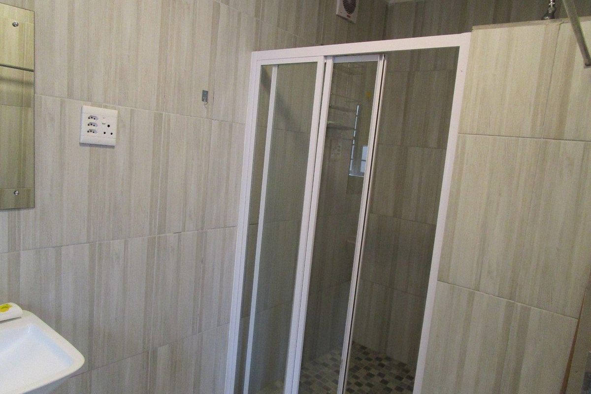 A functional bathroom featuring a walk-in shower with a white frame, tiled walls, and a wall-mounted basin.