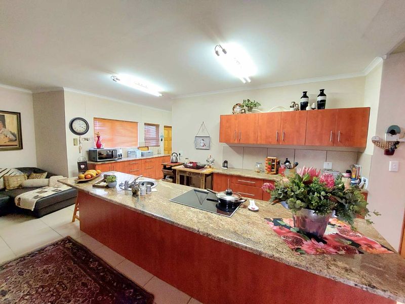 Open-plan kitchen featuring a large granite island with a built-in hob, ample cabinetry, and tiled flooring, seamlessly connecting to the living area.