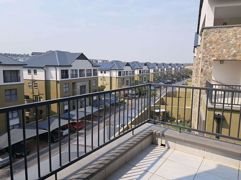 A spacious balcony with tiled flooring and a metal balustrade, offering an elevated view of the apartment complex and parking area.